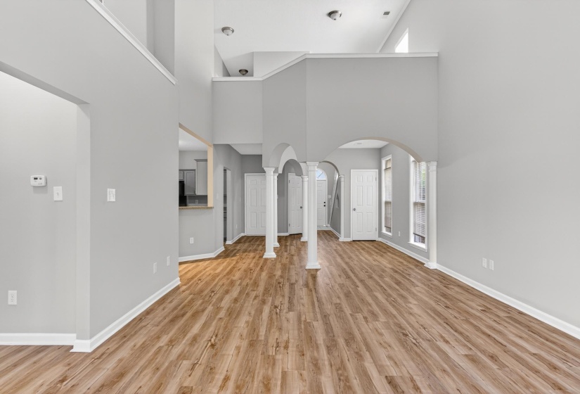 Spacious living area featuring high ceilings, wood-finish flooring, arched doorways, multiple windows, and a balcony overlook
