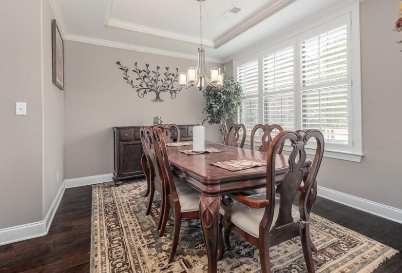 Formal dining space featuring a tray ceiling, crown molding, and plantation shutters