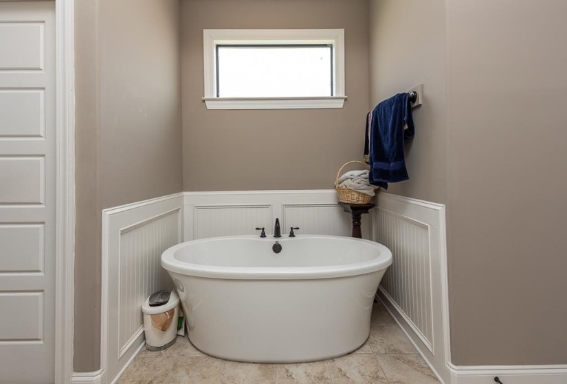 Freestanding soaking tub with matte black fixtures, set against beadboard wainscoting and a neutral wall color