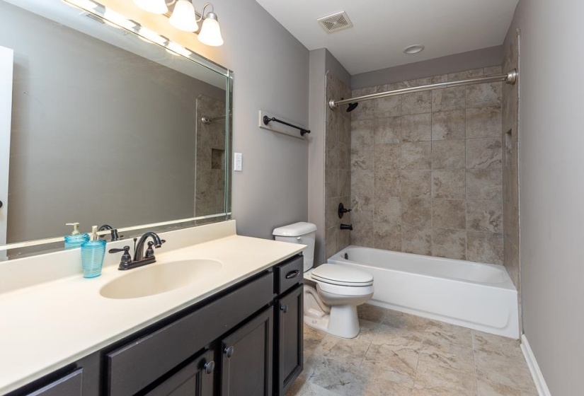 Bathroom featuring a single vanity with dark cabinetry and a light-toned countertop, a large framed mirror, and a tub/shower combination with tile surround