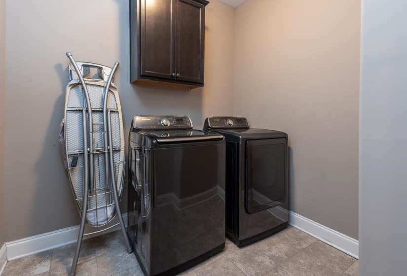 Dedicated laundry space featuring a dark finish upper cabinet, a neutral wall color, and a light-toned flooring