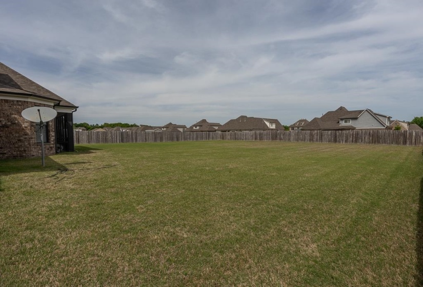 Expansive backyard featuring a large green lawn, full privacy fencing, and brick exterior