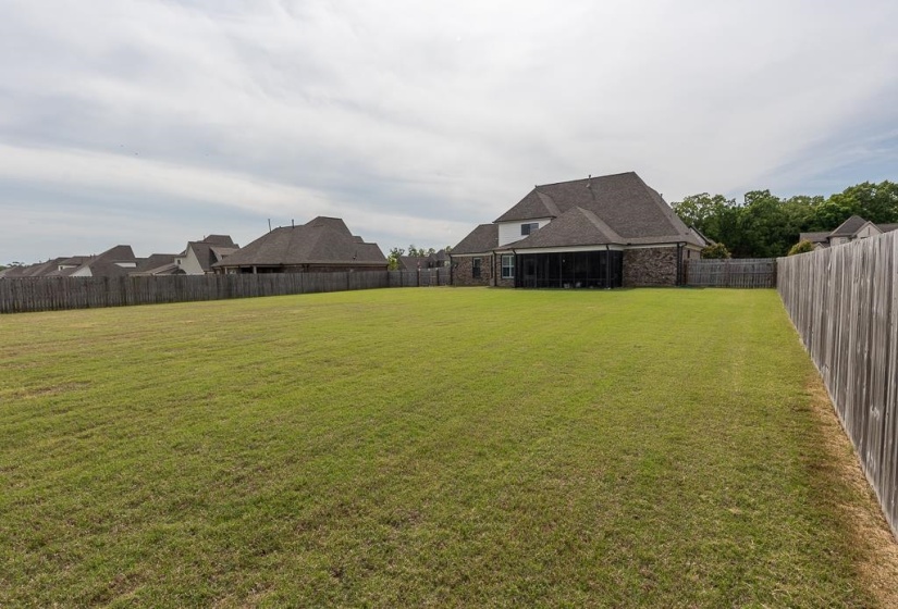 Expansive backyard featuring a large green lawn, full privacy fencing, and a screened-in porch