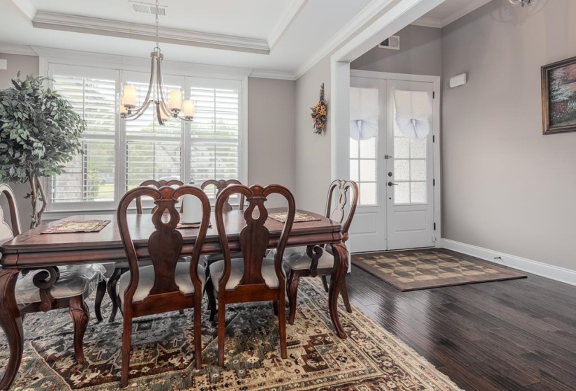 Dining area with dark wood-finish flooring, white plantation shutters, a tray ceiling, and an overhead chandelier