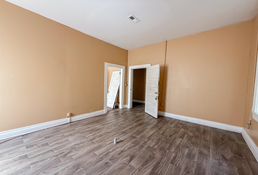 Spacious room featuring wood-look plank flooring, light beige wall paint, white trim, and multiple doorways
