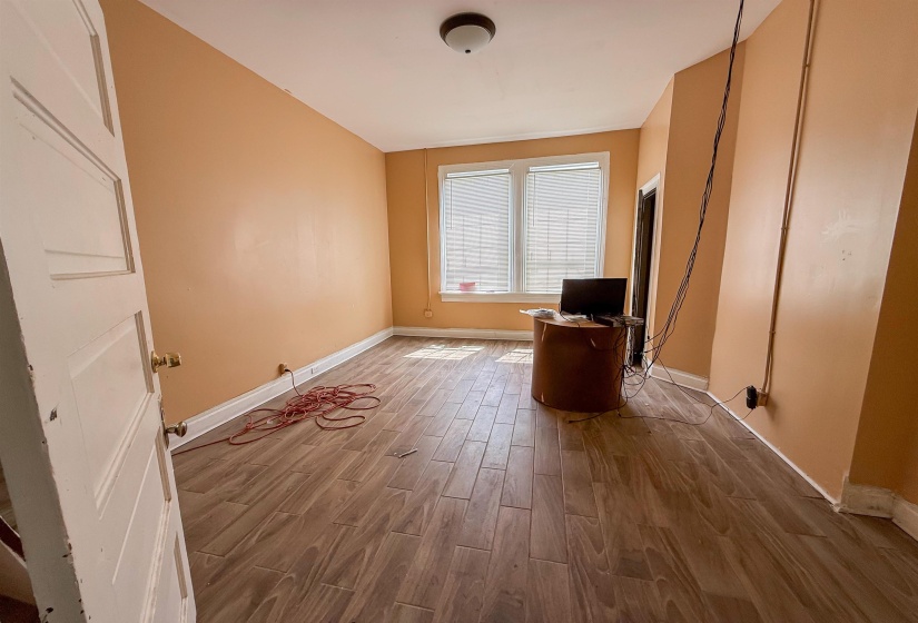 Spacious interior room featuring wood-finish flooring, light-colored walls, and a ceiling-mounted light fixture