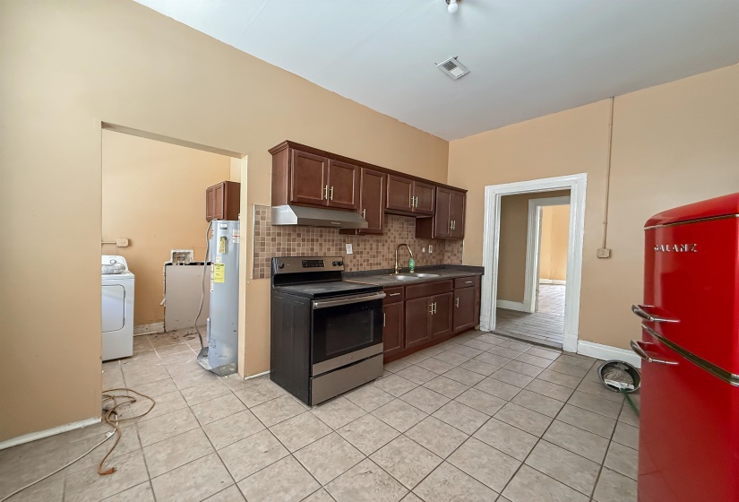 Kitchen featuring tiled flooring, dark wood-finish cabinetry, a stainless steel range, and a mosaic tile backsplash