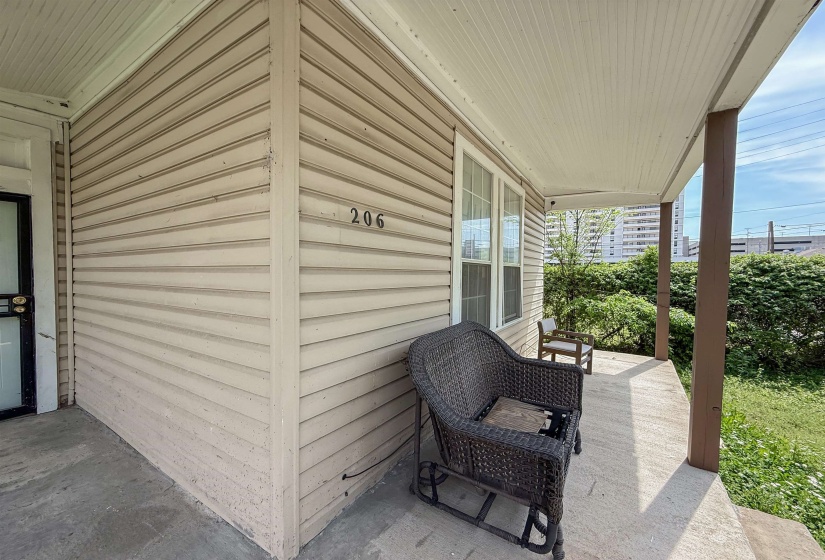 Covered concrete porch featuring a beadboard ceiling, two support pillars, and tan siding