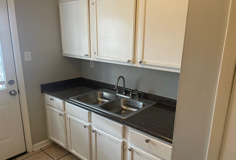 Kitchen with white cabinets, light tile patterned floors, a sink, and dark countertops