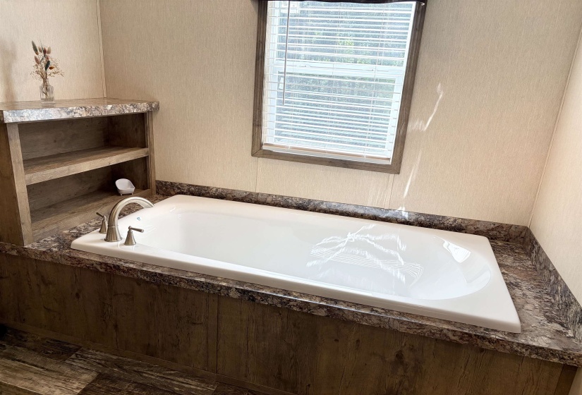 Built-in soaking tub featuring a brushed nickel faucet, a surrounding stone-look countertop, and wood-finish paneling