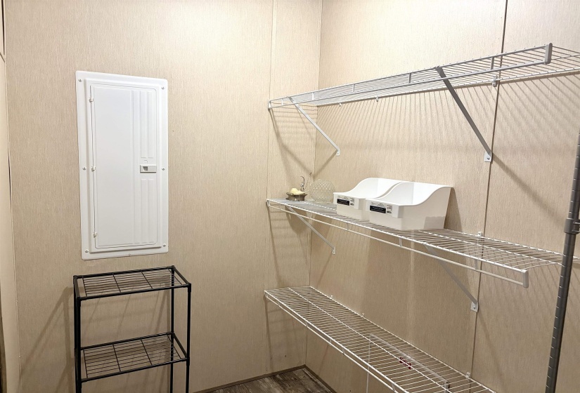 Utility space featuring multiple wire shelving units, a built-in electrical panel, wood-finish flooring, and light-toned wall panels