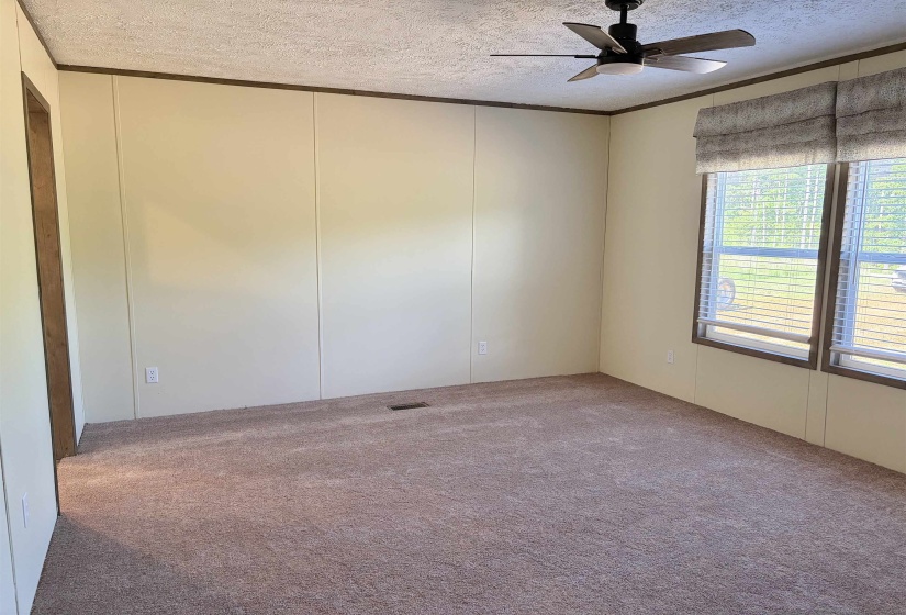 Spacious room featuring neutral wall panels, brown carpet, and a ceiling fan with light fixture