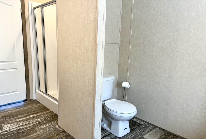 Dedicated water closet with light-toned wall panels, a white toilet, and wood-finish flooring