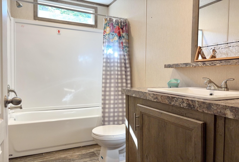 Bathroom featuring a white bathtub and shower combination, wood-finish vanity with a rectangular sink, speckled countertop, and a framed mirror
