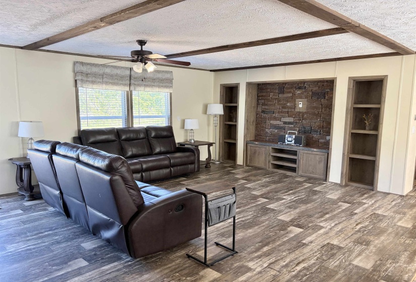 Living area featuring wood-finish flooring, exposed ceiling beams, and a built-in entertainment center with stone accent wall