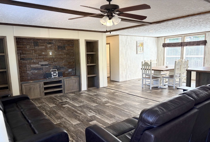 Living area featuring wood-finish flooring, a stone-accented media wall with built-in cabinetry, and integrated shelving
