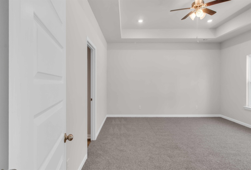 Carpeted empty room featuring a ceiling fan, a raised ceiling, and recessed lighting