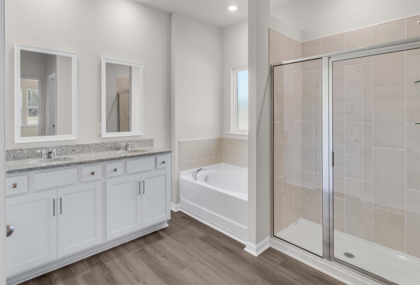 Full bath featuring double vanity, a stall shower, a garden tub, and light wood-style flooring