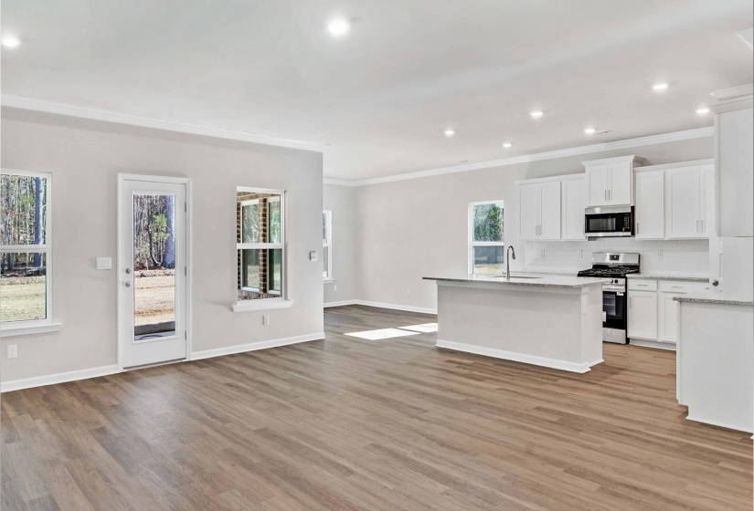 Kitchen featuring stainless steel appliances, white cabinetry, open floor plan, light stone counters, and ornamental molding