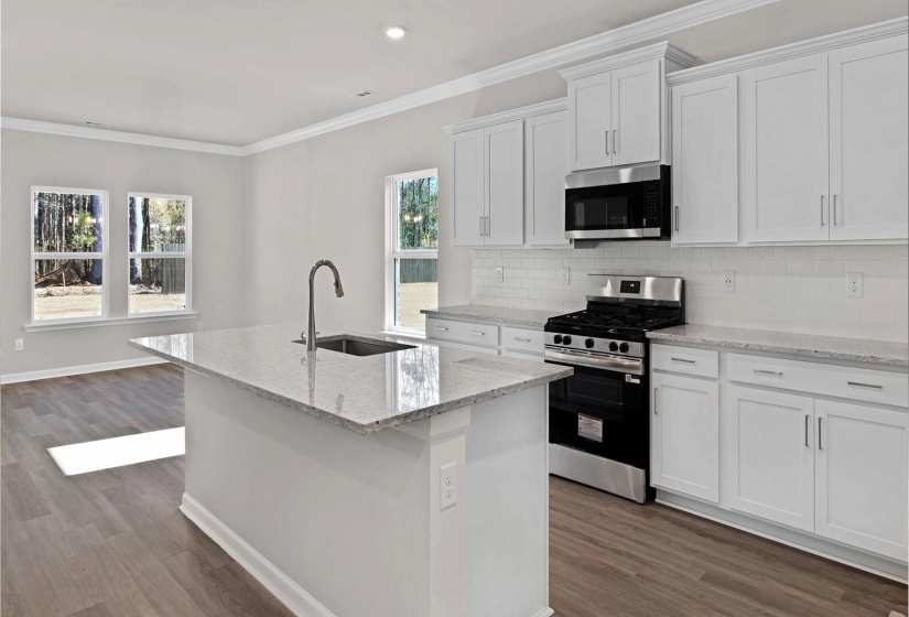 Kitchen featuring stainless steel appliances, white cabinets, ornamental molding, light stone countertops, and decorative backsplash