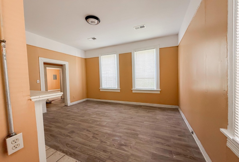 Spacious room featuring wood-finish flooring, two windows with white trim, and a high ceiling with a flush-mount light fixture