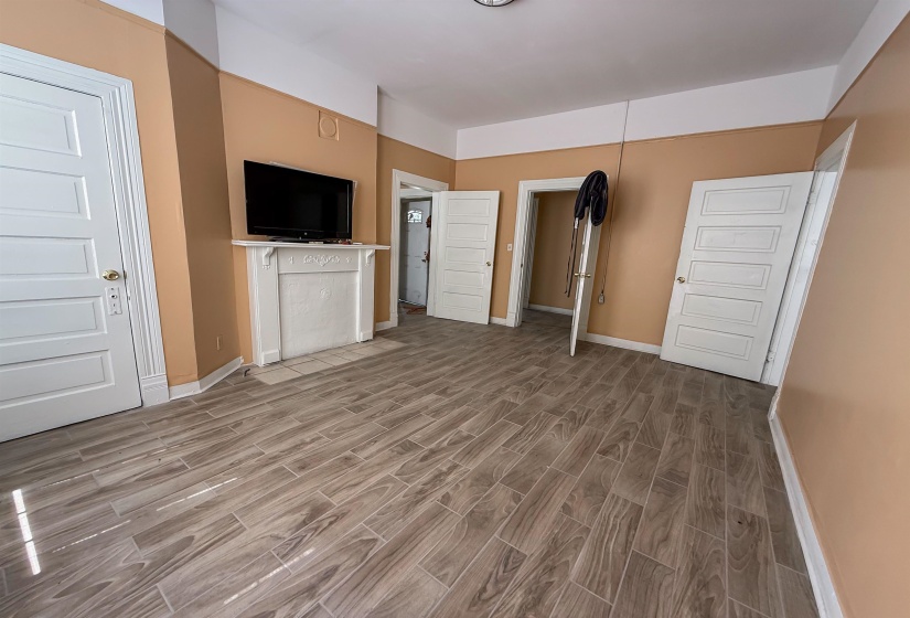 Spacious room featuring wood-finish tile flooring, a decorative white fireplace mantel, and multiple white panel doors