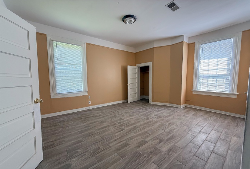 Spacious room featuring wood-finish flooring, two windows with blinds, a built-in closet, and a white paneled door