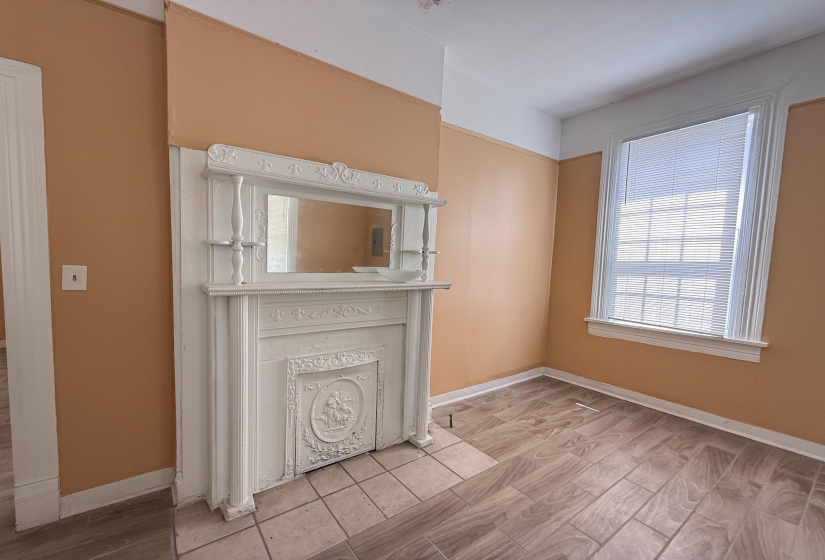 Ornate decorative fireplace mantel with integrated mirror, tile hearth, wood-finish flooring, and a window with blinds