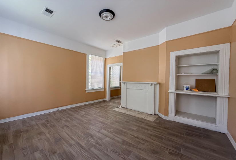 Room with wood-finish flooring, two windows with blinds, a decorative fireplace surround, and built-in shelving