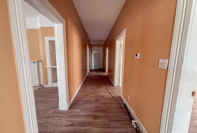 Long hallway featuring wood-finish flooring, light peach walls, and multiple doorways with white trim