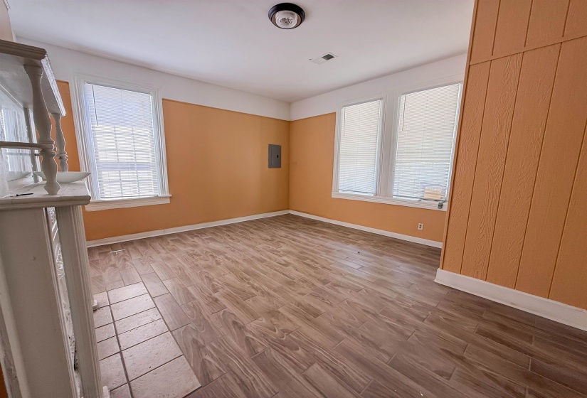 Spacious interior room featuring wood-finish flooring, white trim, and multiple windows with blinds