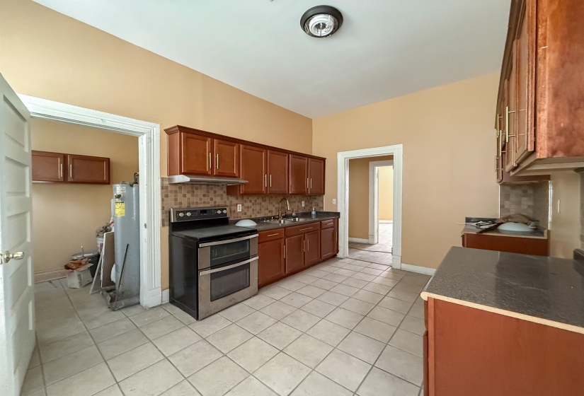 Kitchen featuring tile flooring, wood-finish cabinetry, a tile backsplash, and a double oven range