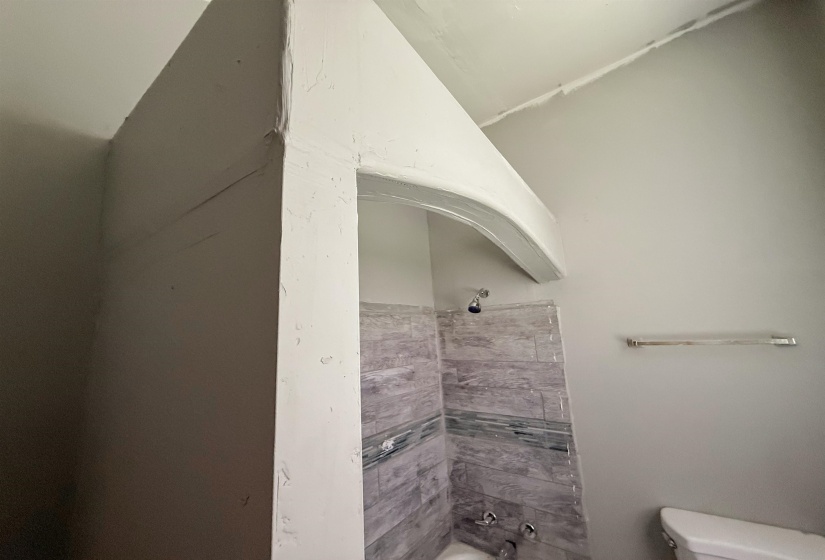 Bathtub with gray and blue-toned tile surround, chrome fixtures, and an adjacent toilet