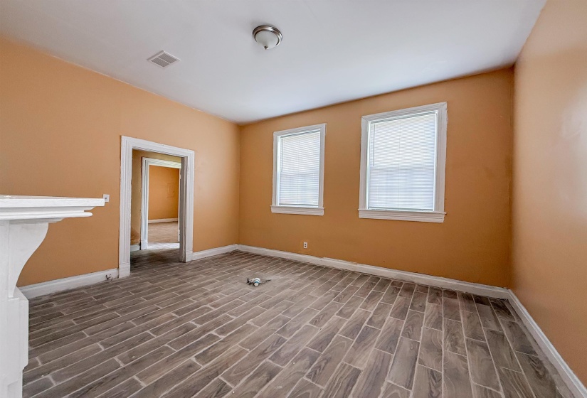 Room featuring wood-finish tile flooring, two windows with white blinds, a white decorative fireplace surround, and a ceiling-mounted light fixture