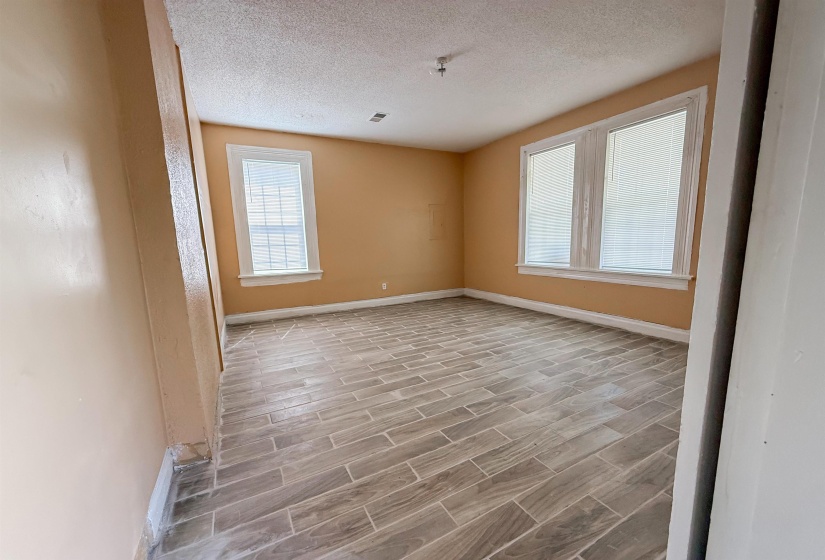 Spacious room featuring wood-finish tile flooring, neutral wall paint, and multiple windows with white trim