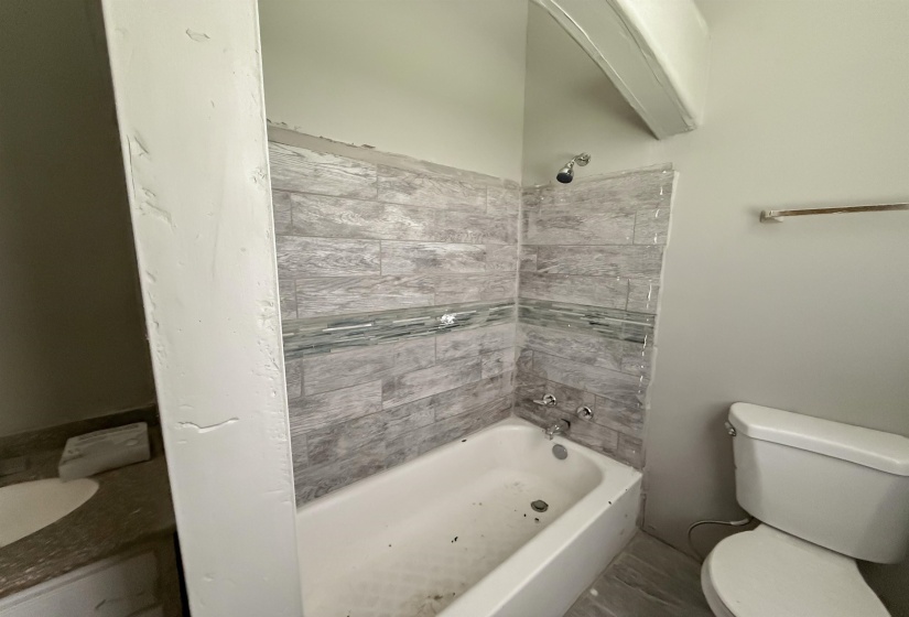 Bathtub with light gray subway tile surround and decorative glass accent band
