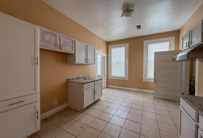Kitchen area featuring white cabinetry with gold-toned hardware, light-toned tiled flooring, and multiple windows