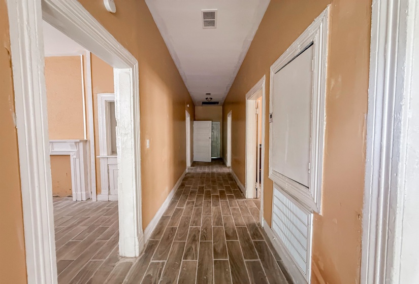 Hallway featuring wood-finish flooring, multiple doorways with white trim, a floor-level vent, and a ceiling-mounted light fixture
