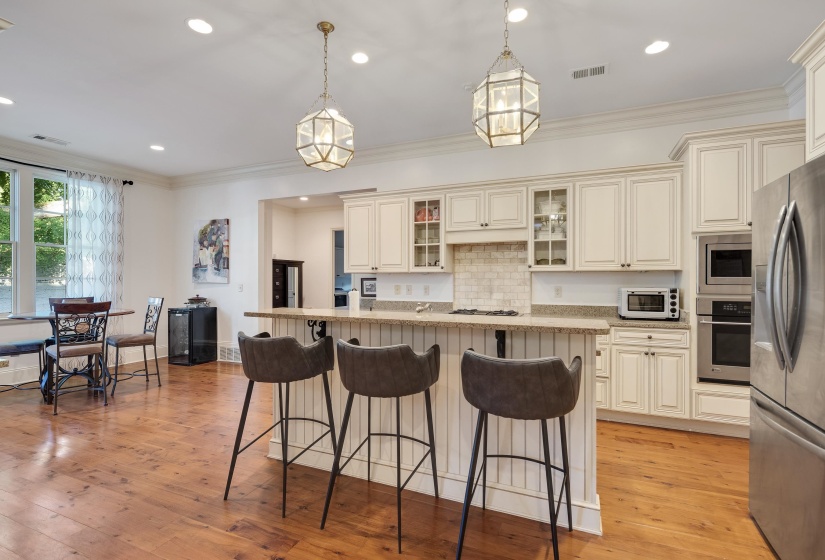 Kitchen featuring wood-finish flooring, white cabinetry, a built-in oven, stainless steel appliances, and a central island with bar seating