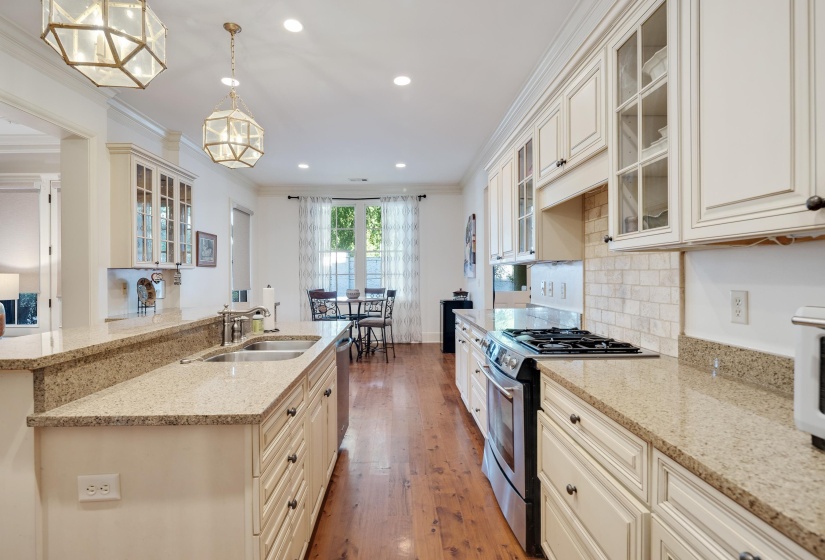 Kitchen featuring light-toned cabinetry with glass-front accents, speckled countertops, stainless steel appliances, and wood-finish flooring