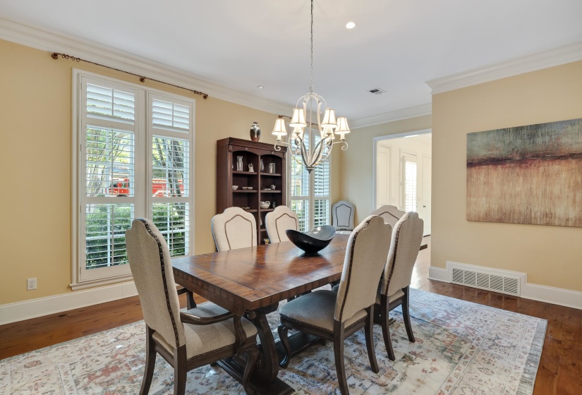 Spacious room with wood-finish flooring, two large windows with plantation shutters, elegant crown molding, and a built-in display cabinet