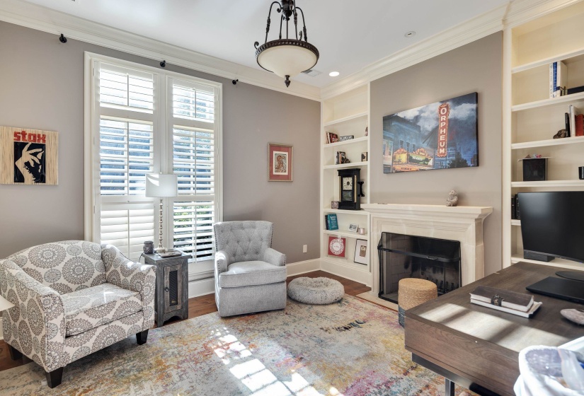 Well-appointed room featuring extensive built-in shelving, a prominent fireplace with a substantial mantel, and a large window fitted with plantation shutters