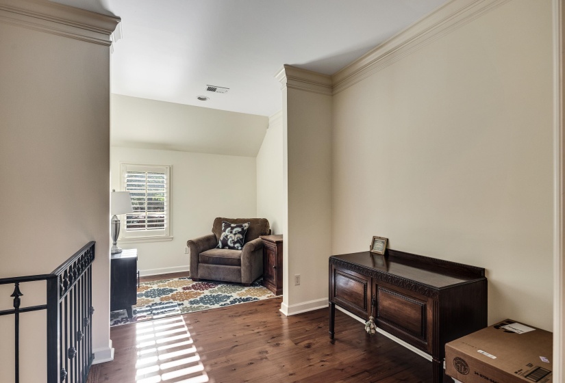 Upper-level landing featuring wood-finish flooring, crown molding, and a wrought iron railing