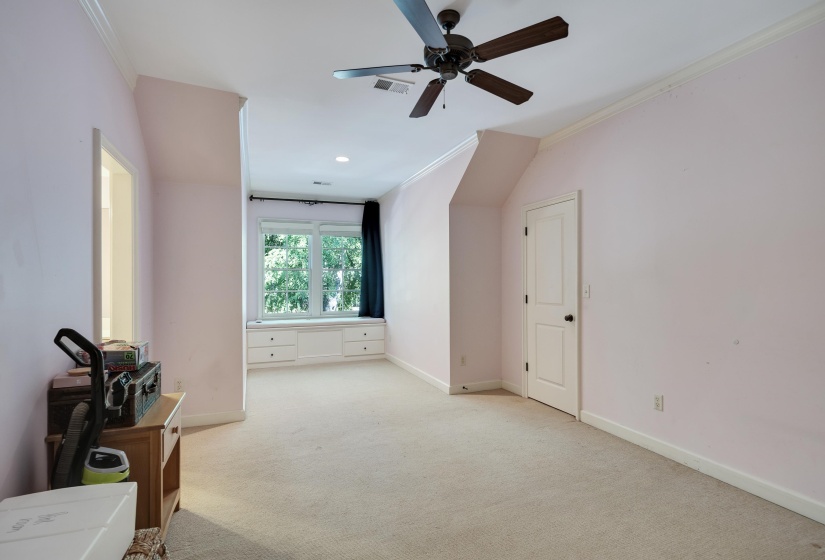 Carpeted room featuring a built-in window seat with storage drawers, a ceiling fan, and crown molding