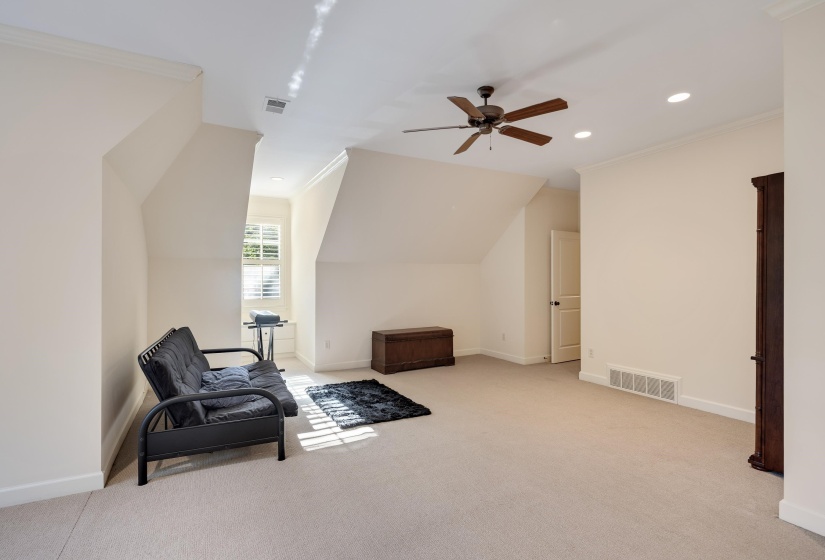 Spacious room featuring sloped ceilings, recessed lighting, a ceiling fan, a window with plantation shutters, and light-toned carpeting