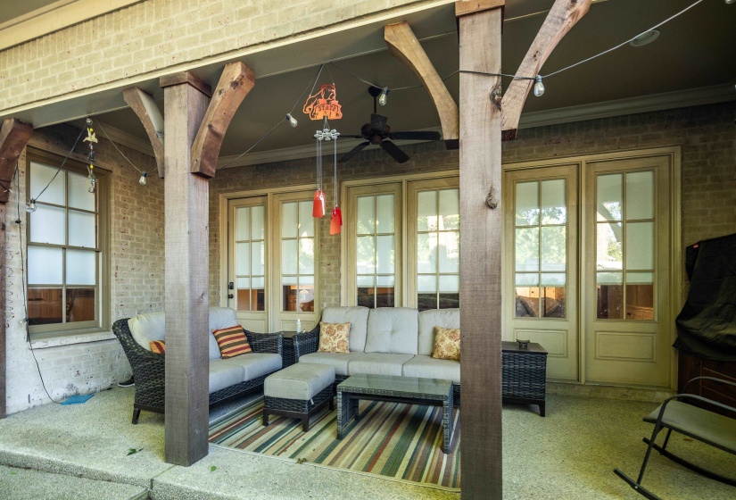 Covered patio featuring exposed timber posts and beams, brick exterior, concrete flooring, and multiple glass-paneled doors