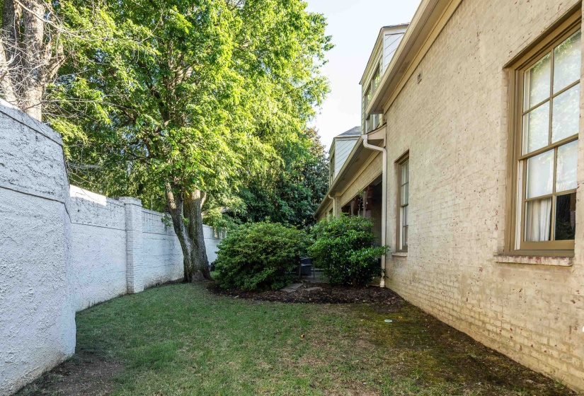 Expansive side yard featuring a manicured lawn, established mature trees, a privacy fence, and brick exterior