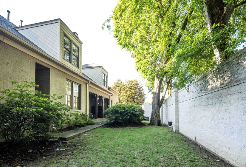 Expansive green lawn bounded by a painted concrete privacy wall and mature trees