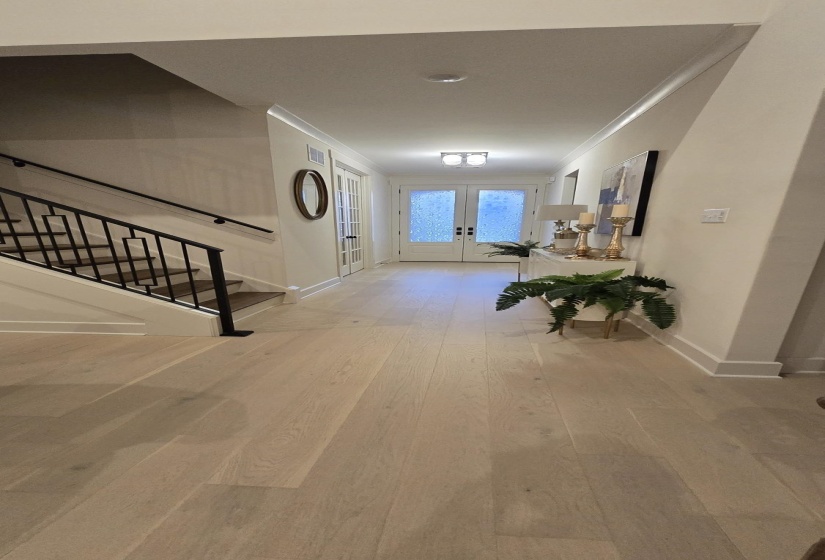 Entryway featuring light wood-finish flooring, white double French doors with frosted glass, and a staircase with black metal railings and wood treads