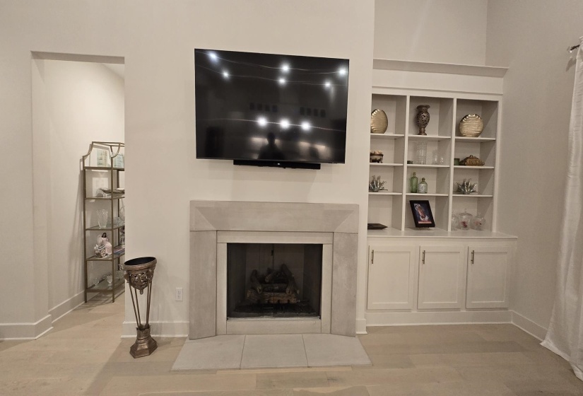 Stone-clad fireplace with hearth, flanked by built-in shelving and cabinetry, and set on wood-finish flooring